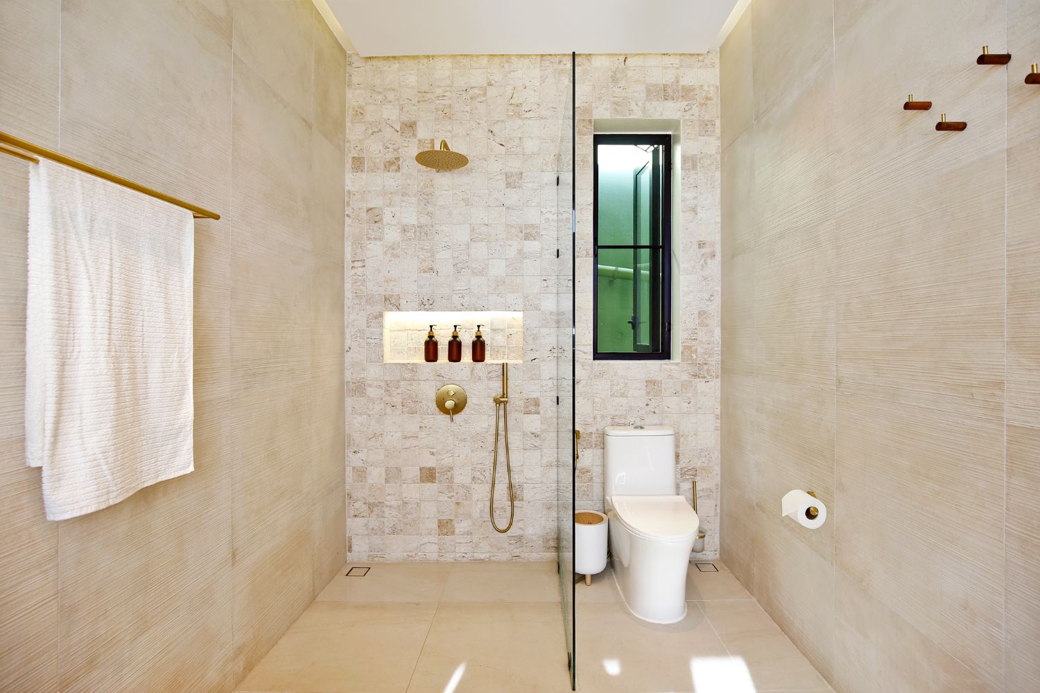 Bathroom in warm travertine with a walk-in rain shower, brass fittings and a slot window into the greenery