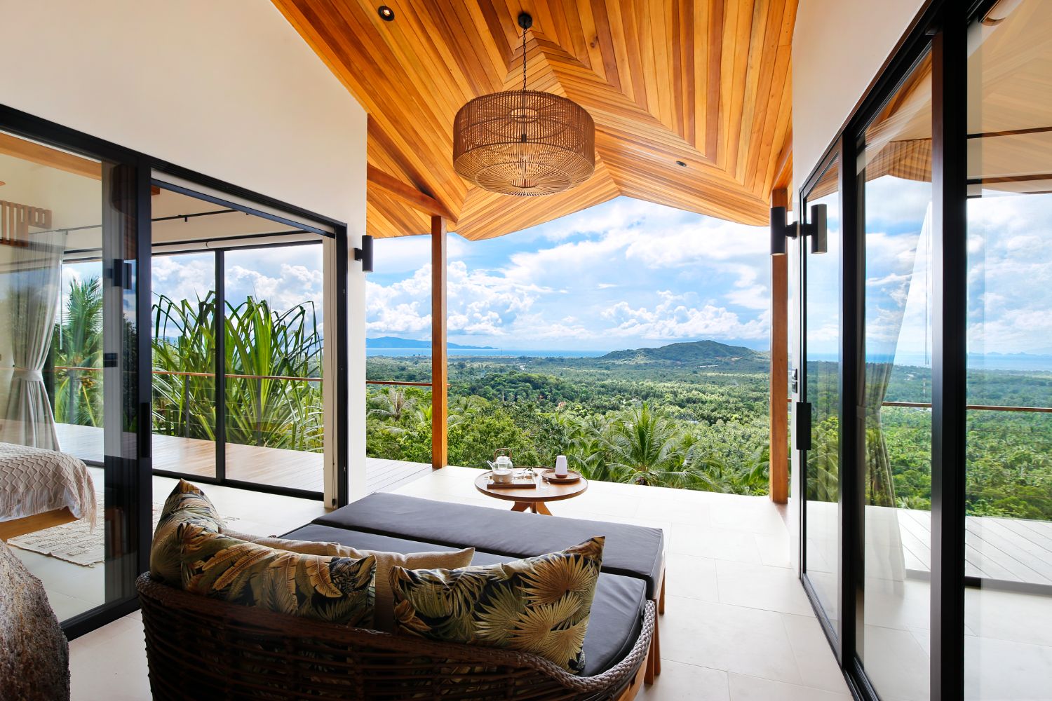 Daybed on a terrace under a woven pendant, looking out over the treetops to the hills and the bay