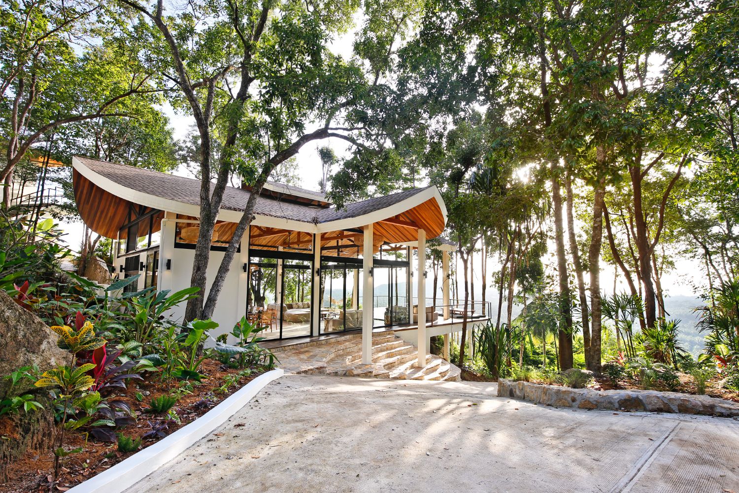 The curved-roof pavilion seen from the stone drive, surrounded by trees and planting