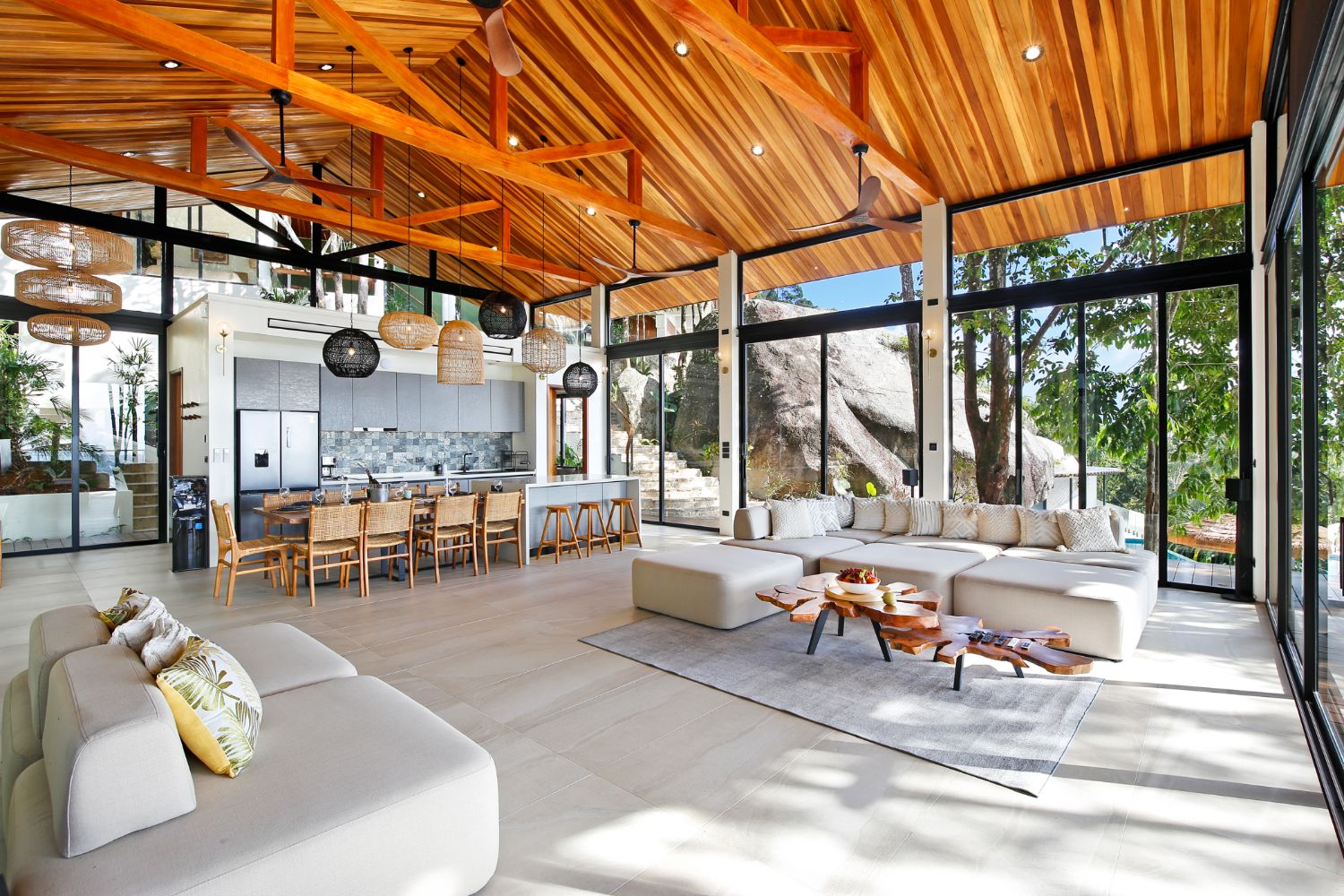 Open-plan living and kitchen under the raked teak roof, breakfast bar with stools and sofas around a low table