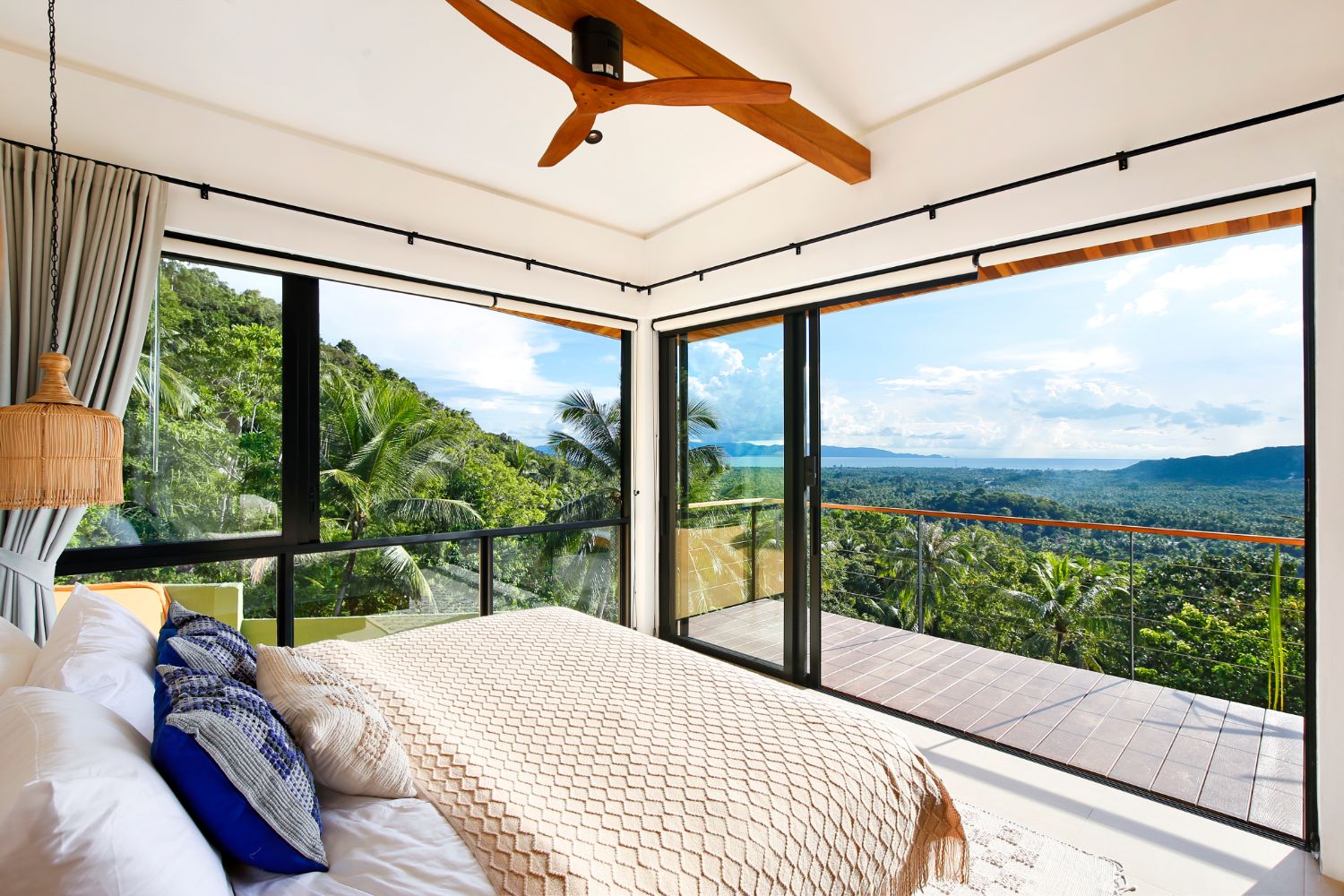 Bedroom with a white linen bed facing floor-to-ceiling glass and a private terrace over the jungle and the bay