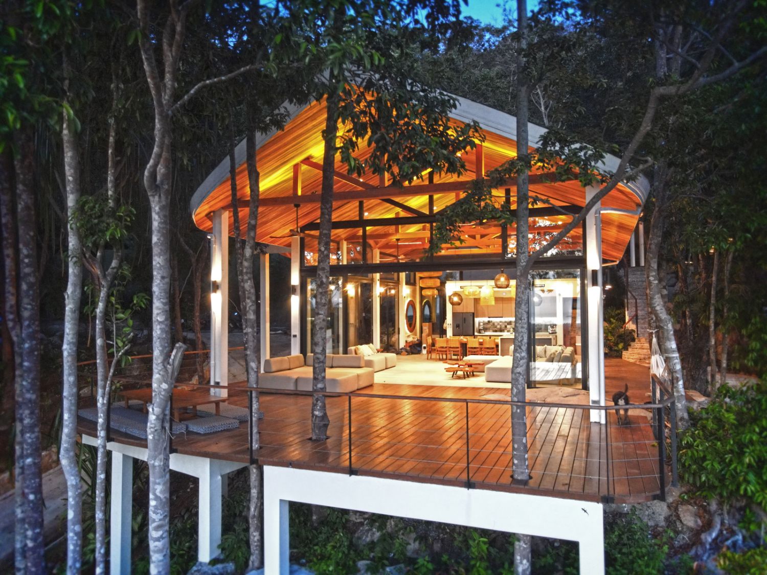 A pavilion lit warm at night on its raised teak deck among the trees