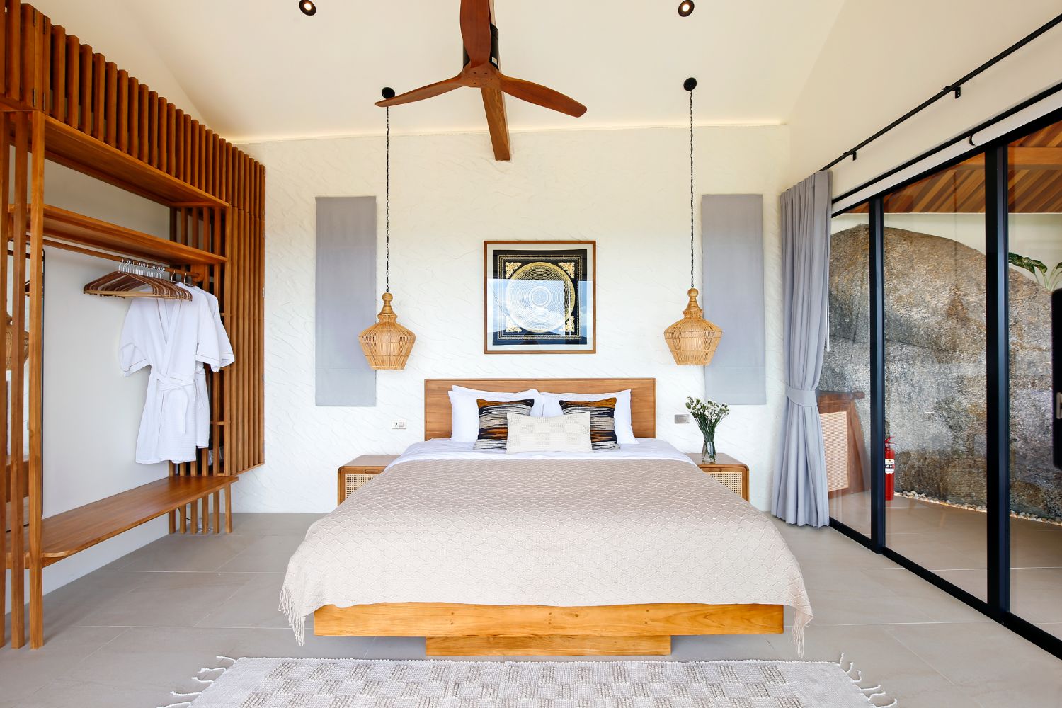 Bedroom with a low teak bed, two woven pendant lamps and an open teak wardrobe with robes