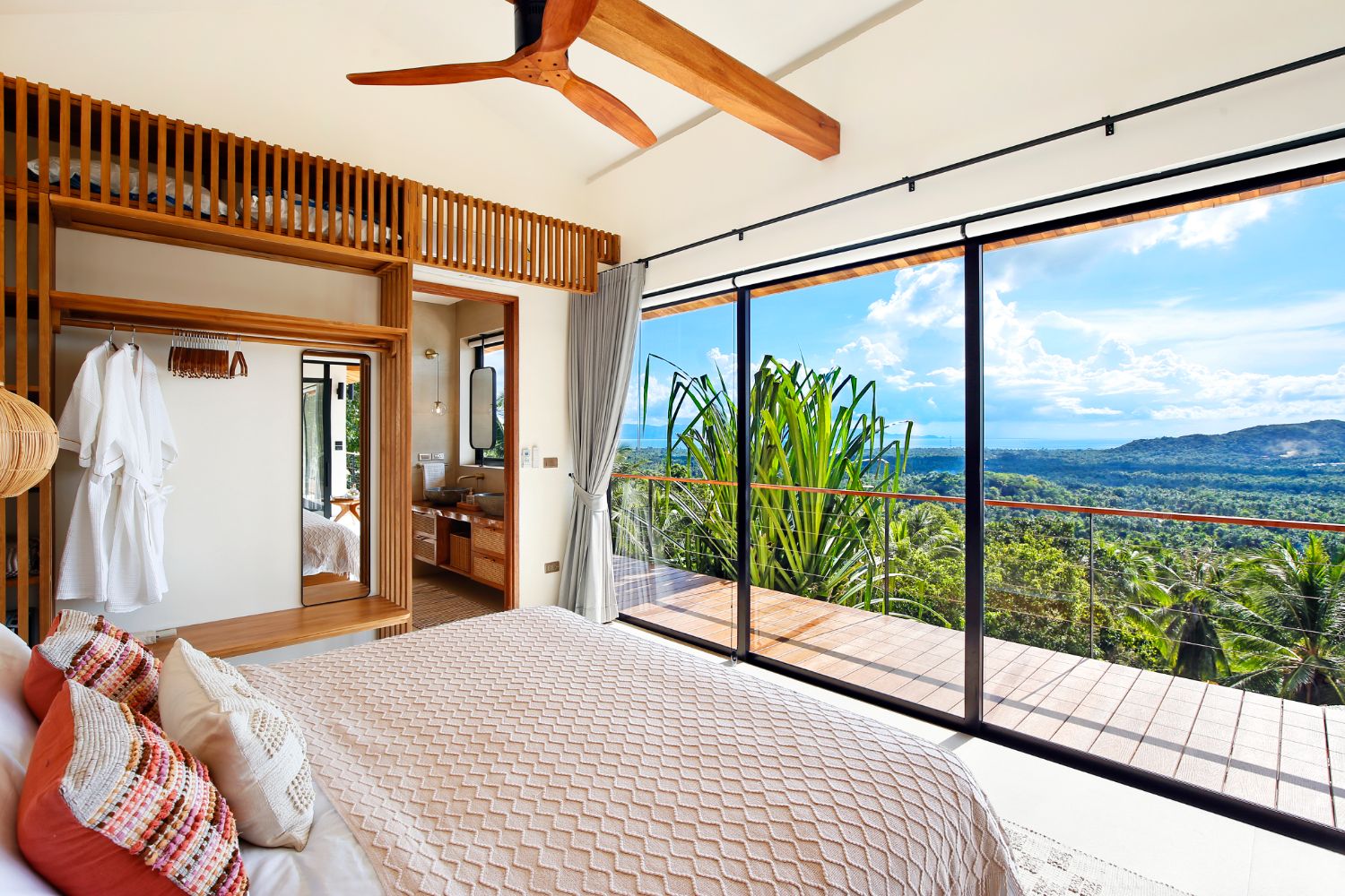 Bedroom with an open wardrobe and a bathroom behind, wide sliding doors onto the deck and the sea view