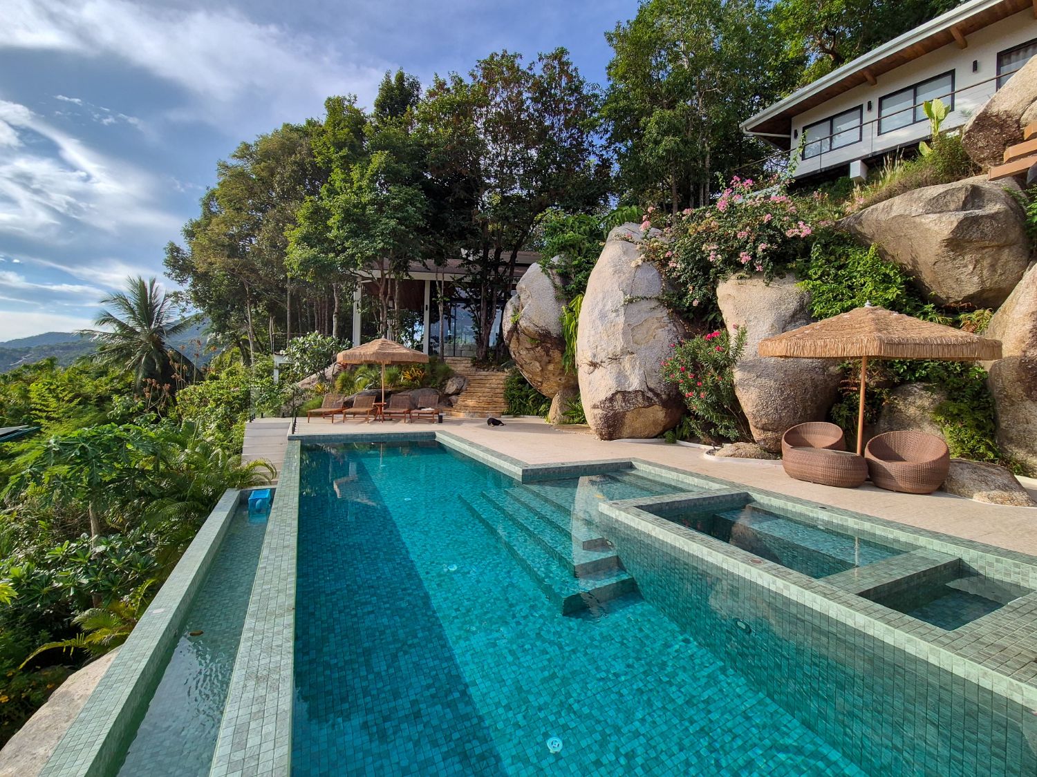 The pool and jacuzzi running between granite boulders, thatched parasols on the terrace and hills in the distance