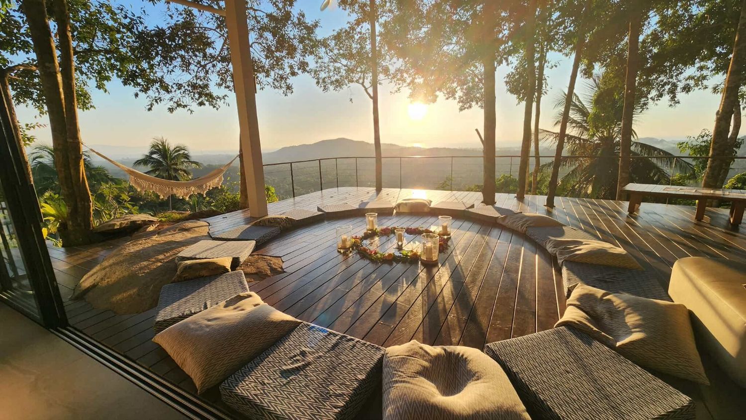 The round timber sun deck at Villa Ullassa laid out with cushions at sunset, open to the treetops and the sea