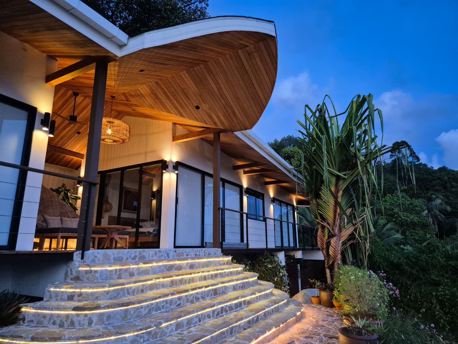 The curved timber-soffit roof and lit stone steps of the main pavilion at blue hour