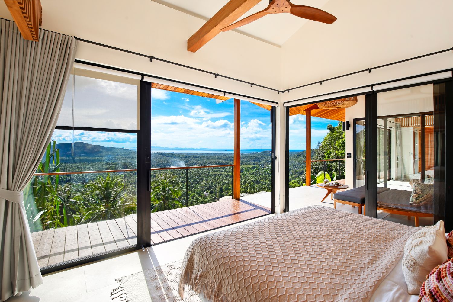 Bedroom opening onto a wide corner of glass with the bay and the hills filling the view
