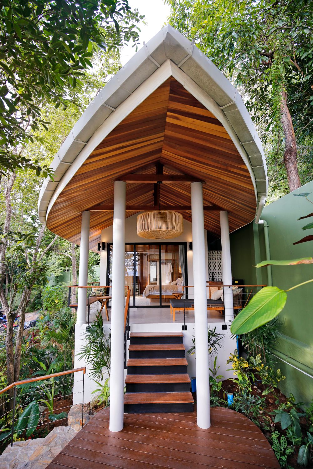 The pointed teak-lined roof of one of the villa's buildings above a colonnade and steps, framed by jungle