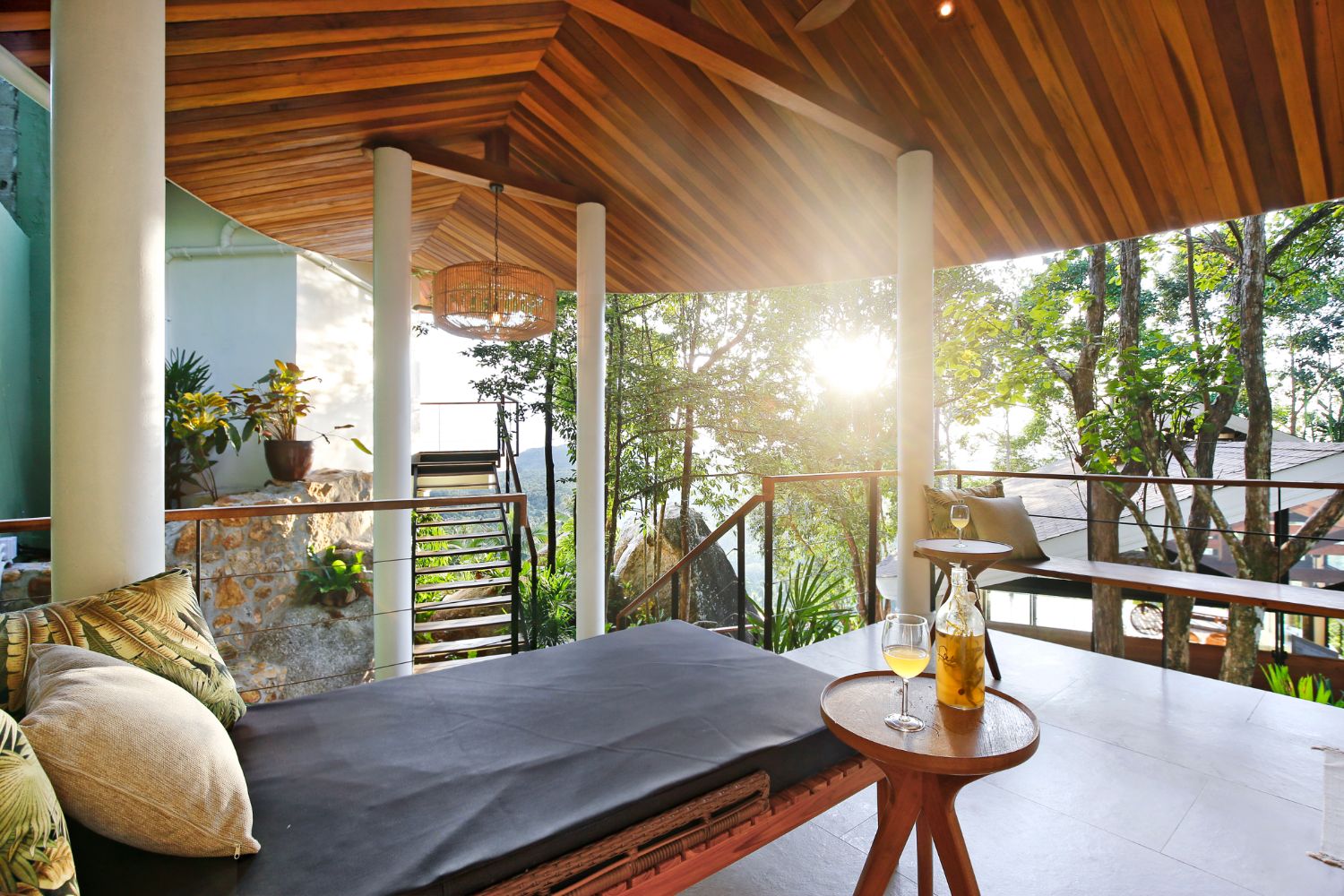 Daybed on a covered terrace with the low sun coming through the trees behind the railing