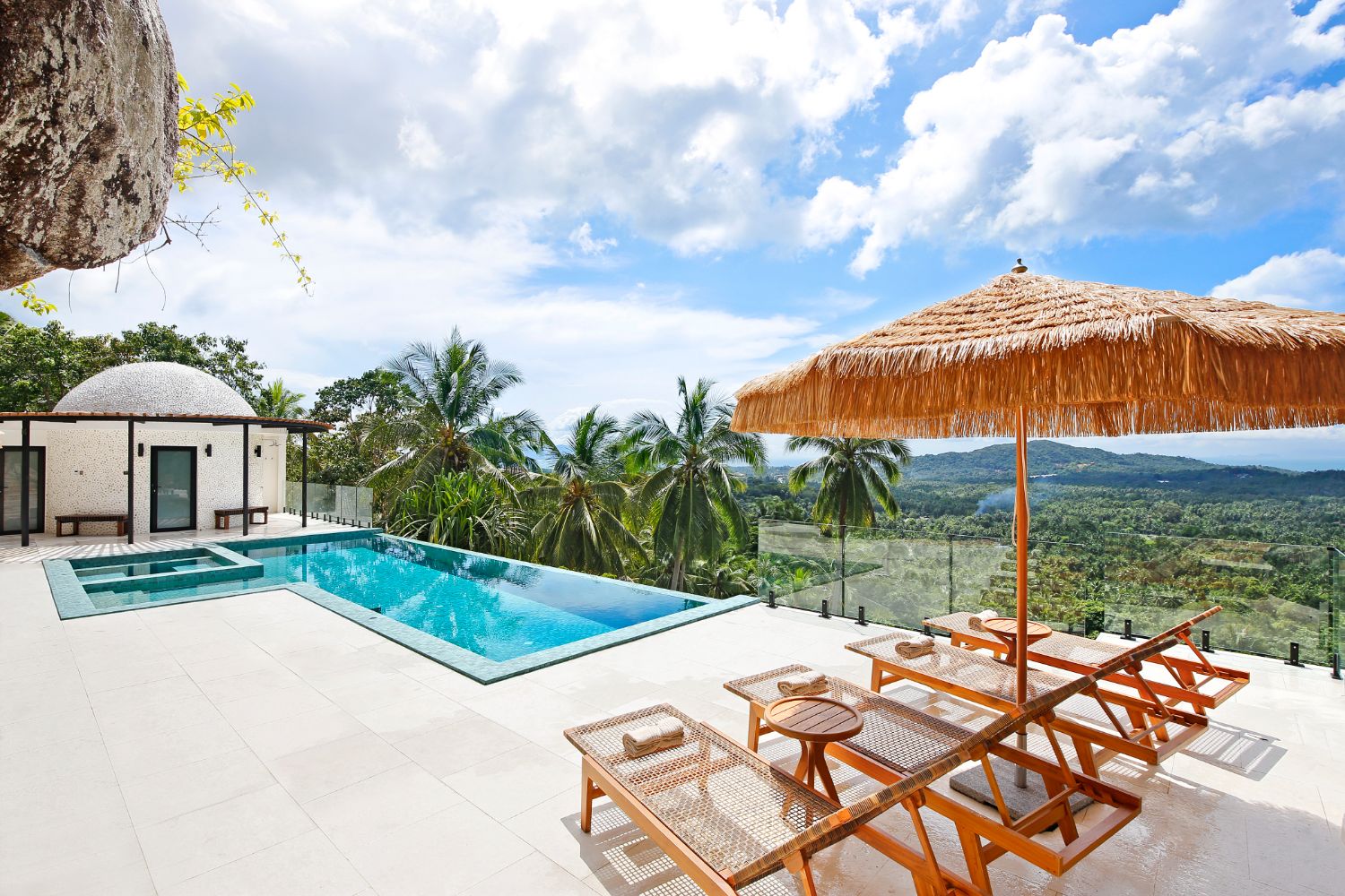 The pool terrace by day: thatched parasol, teak loungers, the dome to one side and a wide view over the island