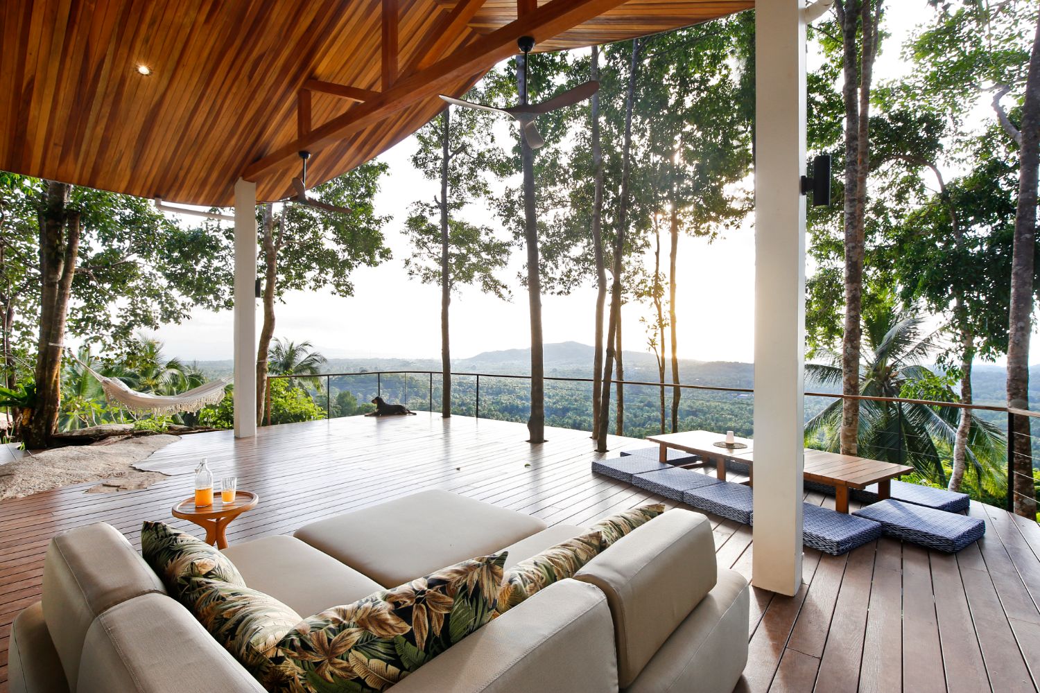 Covered terrace lounge with deep sofas, a hammock and a low table on the deck, open to the canopy and the horizon