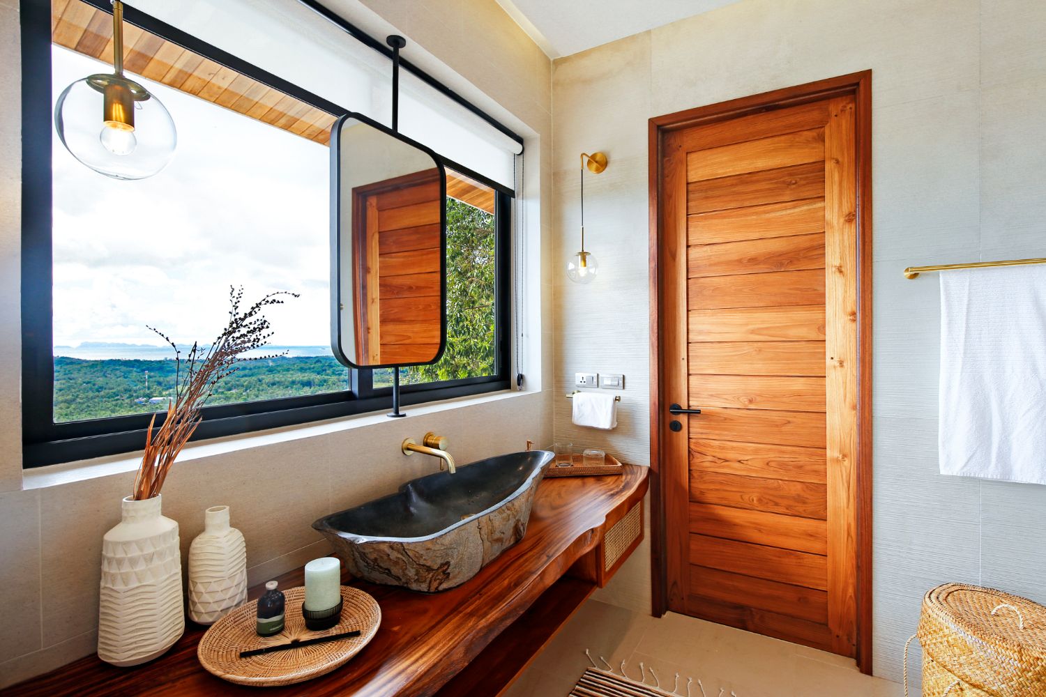 Bathroom with a dark stone basin on a live-edge teak counter, a round mirror and a solid teak door